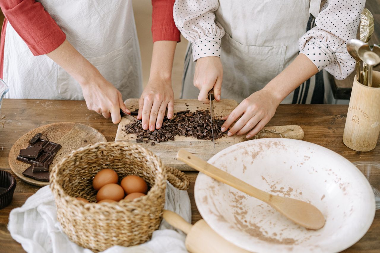 journey-02 Close-up of hands chopping chocolate with eggs and baking ingredients on a wooden table.