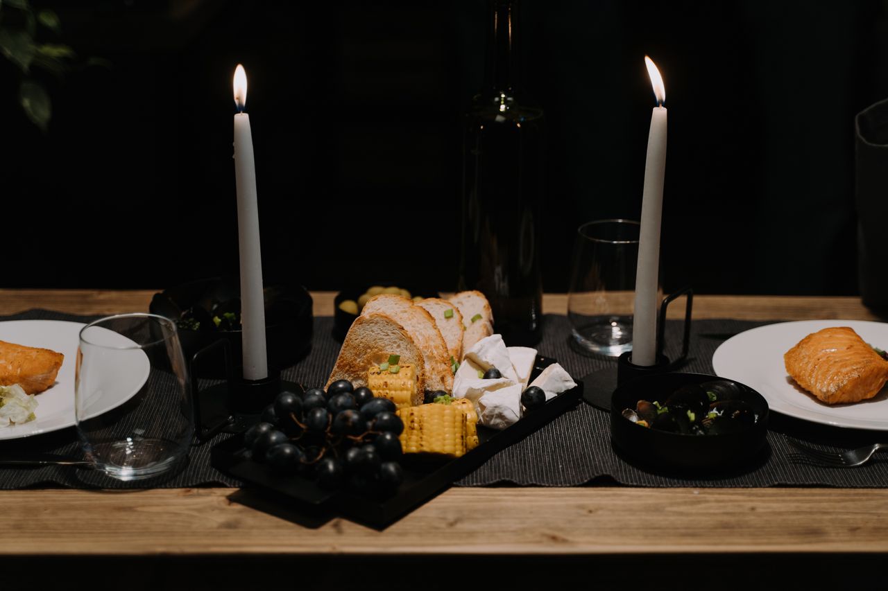 about-img A romantic candlelit dinner setup featuring salmon, cheese, bread, and grapes for an intimate meal.
